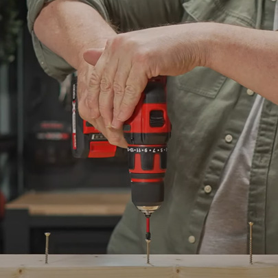  A man is screwing screws into a board with a cordless screwdriver